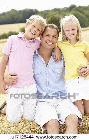 Picture - Father And Children Sitting On Straw Bales In Harvested Field. Fotosearch