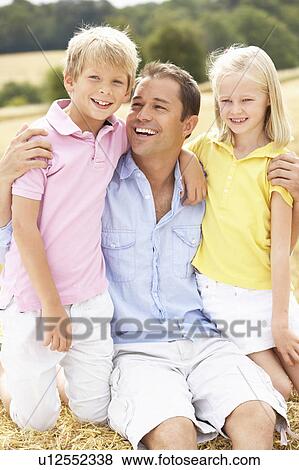 Stock Photo - Father And Children Sitting On Straw Bales In Harvested Field. Fotosearch