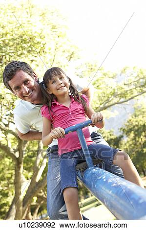 Stock Image - Father And Daughter Riding On See Saw In Playground. Fotosearch