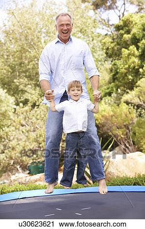 Stock Image - Father And Son Jumping On Trampoline In Garden. Fotosearch