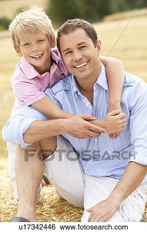Stock Photograph - Father And Son Sitting On Straw Bales In Harvested Field. Fotosearch