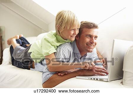 Stock Image - Father And Son Using Laptop Relaxing Sitting On Sofa At Home. Fotosearch