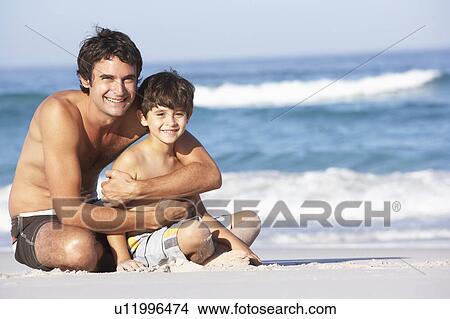Picture - Father And Son Wearing Swimwear Sitting On Sandy Beach. Fotosearch