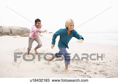 Stock Image - Father Chasing Son Along Winter Beach. Fotosearch
