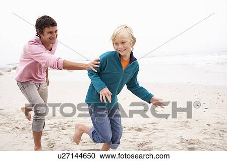Stock Image - Father Chasing Son Along Winter Beach. Fotosearch