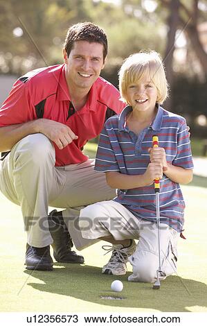 Stock Image - Father Teaching Son To Play Golf On Putting On Green. Fotosearch
