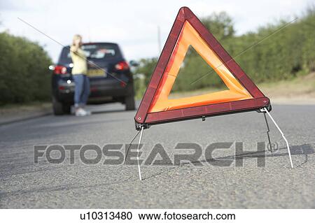 Stock Image - Female Driver Broken Down On Country Road With Hazard Warning Sign In Foreground. Fotosearch