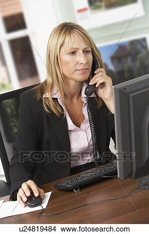 Picture - Female Estate Agent Talking On Phone At Desk. Fotosearch