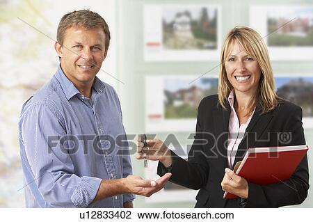 Stock Image - Female Estate Handing Over Keys Of New Home To Client. Fotosearch