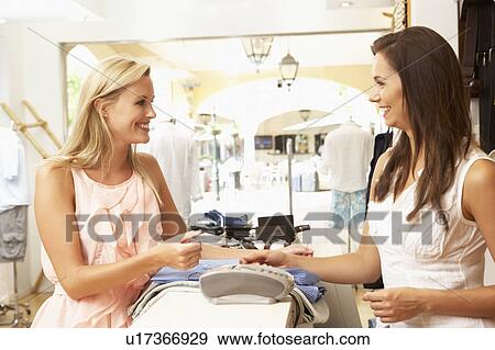Stock Photo - Female Sales Assistant At Checkout Of Clothing Store With Customer. Fotosearch