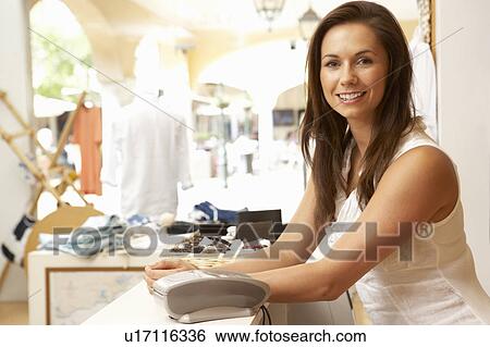 Stock Photograph - Female Sales Assistant At Checkout Of Clothing Store. Fotosearch