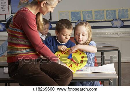 Stock Image - Female Teacher In Primary School Teaching Children To Tell Time In Classroom. Fotosearch