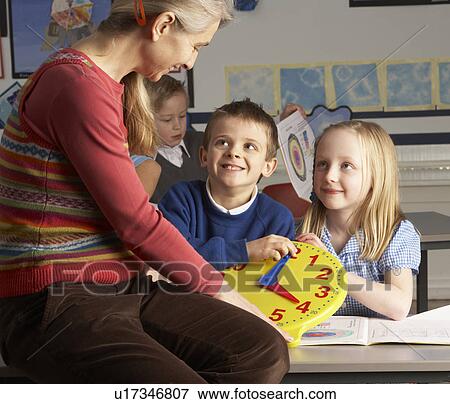 Stock Photo - Female Teacher In Primary School Teaching Children To Tell Time In Classroom. Fotosearch