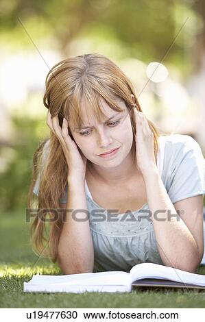 Stock Image - Female Teenage Student Studying In Park Looking Puzzled. Fotosearch