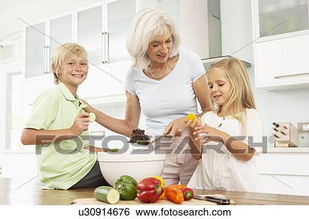 Stock Photograph - Grandchildren Helping Grandmother To Prepare Salad In Modern Kitchen. Fotosearch