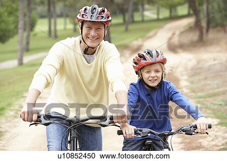 Stock Image - Grandfather and grandson riding bicycle in park. Fotosearch