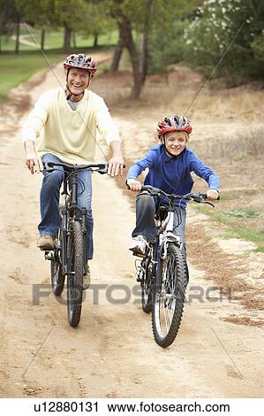 Stock Image - Grandfather and grandson riding bicycle in park. Fotosearch