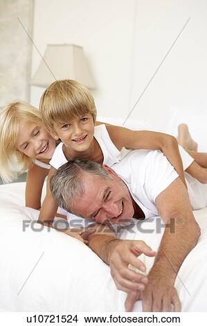 Picture - Grandfather Relaxing On Bed With Grandchildren. Fotosearch