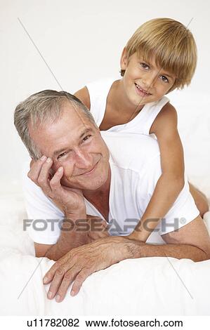 Stock Image - Grandfather Relaxing On Bed With Grandson. Fotosearch
