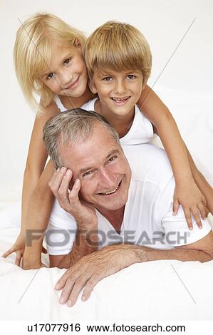 Grandfather Relaxing On Bed With Grandchildren View Large Photo Image Stock Photograph - Grandfather Relaxing On Bed With Grandchildren. Fotosearch
