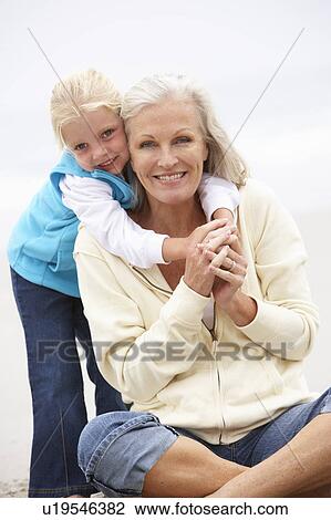 Stock Image - Grandmother And Granddaughter On Holiday Sitting On Winter Beach. Fotosearch