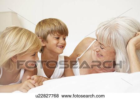 Grandmother Relaxing On Bed With Grandchildren View Large Photo Image Stock Photo - Grandmother Relaxing On Bed With Grandchildren. Fotosearch