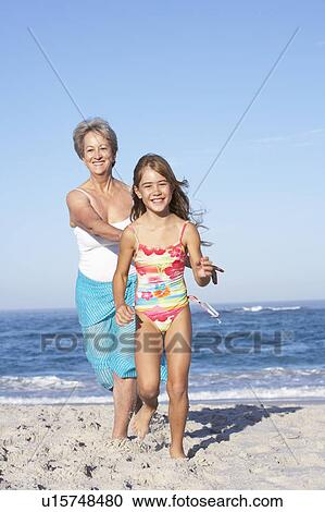 Stock Image - Grandmother Running With Granddaughter Along Sandy Beach. Fotosearch