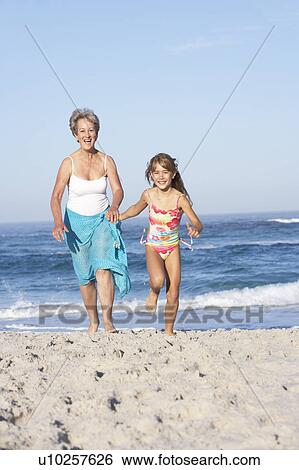 Stock Photograph - Grandmother Running With Granddaughter Along Sandy Beach. Fotosearch