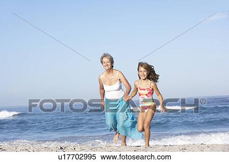 Stock Photography - Grandmother Running With Granddaughter Along Sandy Beach. Fotosearch