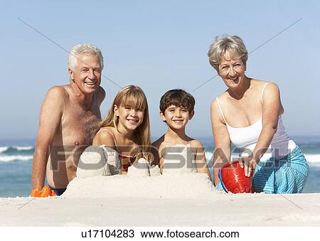 Stock Image - Grandparents And Grandchildren Building Sandcastles Together On Beach Holiday. Fotosearch
