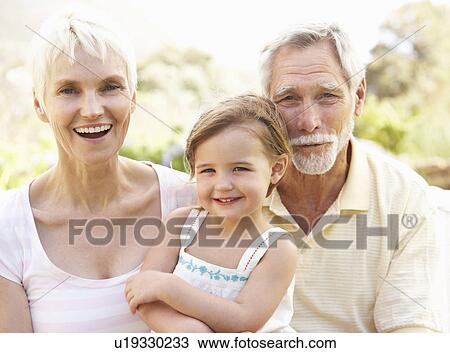 Stock Image - Grandparents And Granddaughter Relaxing In Garden. Fotosearch