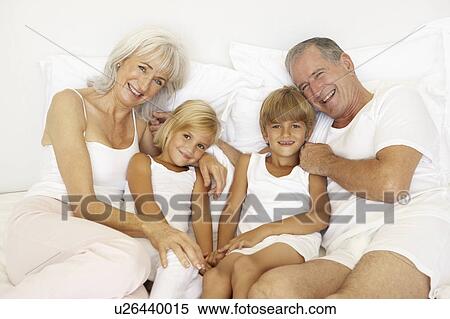 Stock Photography - Grandparents Relaxing On Bed With Grandchildren. Fotosearch