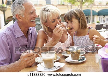 Stock Image - Grandparents With Granddaughter Enjoying Coffee And Cake In Café. Fotosearch