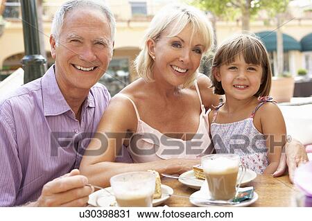 Stock Image - Grandparents With Granddaughter Enjoying Coffee And Cake In Café. Fotosearch