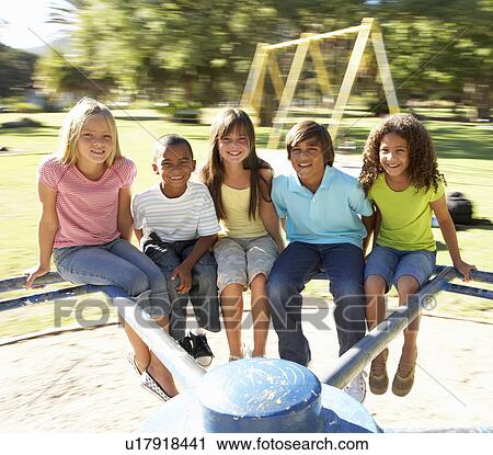 Stock Image - Group Of Children Riding On Roundabout In Playground. Fotosearch