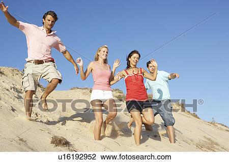 Stock Image - Group Of Friends Enjoying Beach Holiday Running Down Dunes. Fotosearch