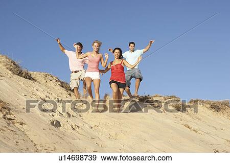Stock Photo - Group Of Friends Enjoying Beach Holiday Running Down Dunes. Fotosearch