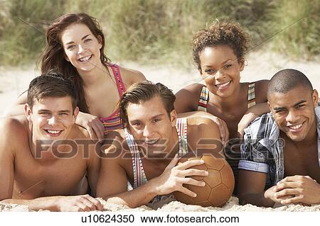 Stock Image - Group Of Friends Relaxing On Beach With Football Together. Fotosearch