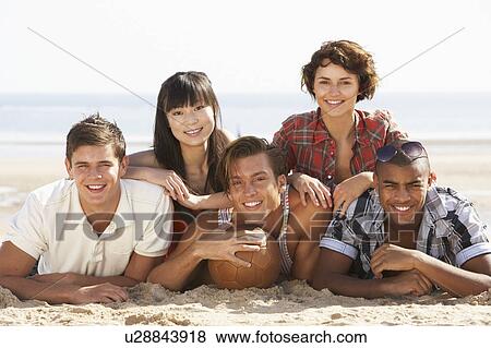 Stock Photo - Group Of Friends Relaxing On Beach With Football Together. Fotosearch