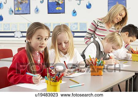 Stock Image - Group Of Primary Schoolchildren And Teacher Having lesson In Classroom. Fotosearch