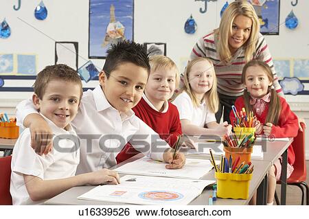 Stock Photograph - Group Of Primary Schoolchildren And Teacher Working At Desks In Classroom. Fotosearch