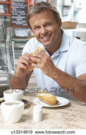 Stock Photo - Male Customer Enjoying Sandwich And Coffee In Café . Fotosearch