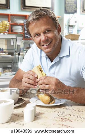 Stock Photography - Male Customer Enjoying Sandwich And Coffee In Café . Fotosearch
