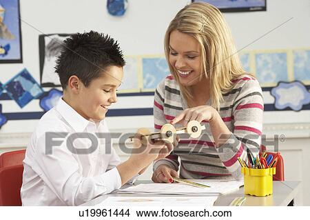 Picture - Male Primary School Pupil And Teacher Working At Desk In Classroom. Fotosearch