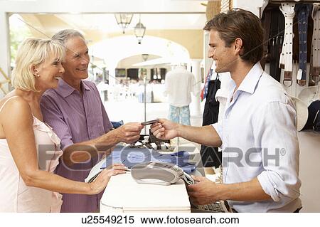 Stock Photography - Male Sales Assistant At Checkout Of Clothing Store With Customers. Fotosearch