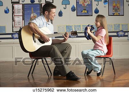 Stock Image - Male Teacher Playing Guitar With Pupil In Classroom. Fotosearch