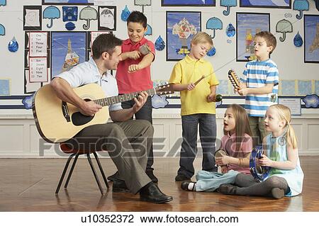 Stock Image - Male Teacher Playing Guitar With Pupils Having Music Lesson In Classroom. Fotosearch