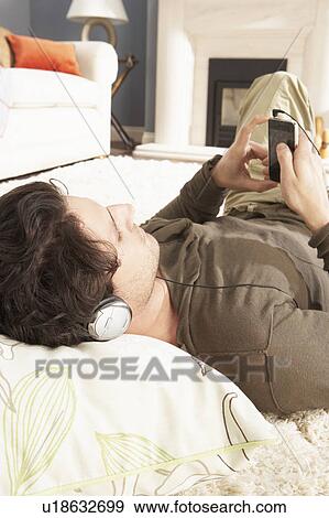 Man Listening To MP3 Player On Headphones Relaxing Laying On Rug At Home View Large Photo Image Stock Photo - Man Listening To MP3 Player On Headphones Relaxing Laying On Rug At Home . Fotosearch