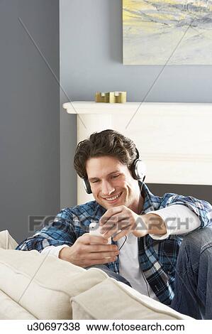 Stock Photo - Man Listening To MP3 Player On Headphones Relaxing Sitting On Sofa At Home . Fotosearch
