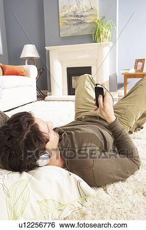 Man Listening To MP3 Player On Headphones Relaxing Laying On Rug At Home View Large Photo Image Stock Photograph - Man Listening To MP3 Player On Headphones Relaxing Laying On Rug At Home . Fotosearch